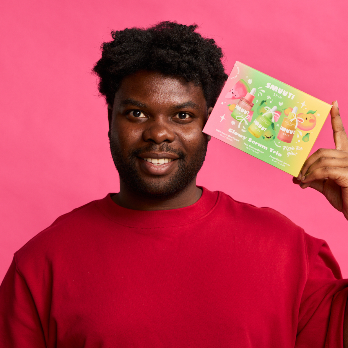 A smiling man in a red sweatshirt holds the Smuuti Skin Glowy Serum Trio