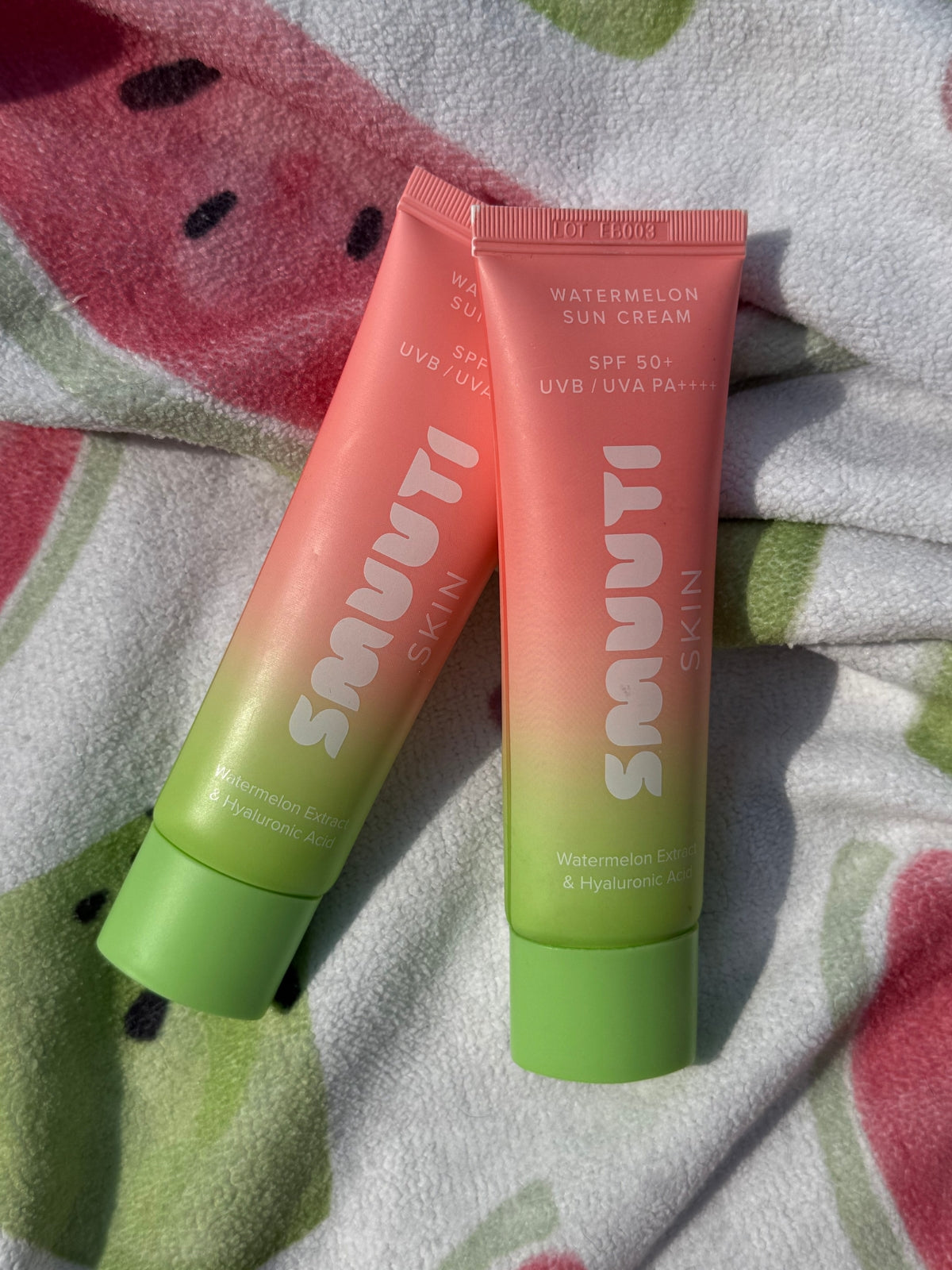 Two tubes of Smuuti Skin watermelon sun cream on a fabric background with watermelon patterns.
