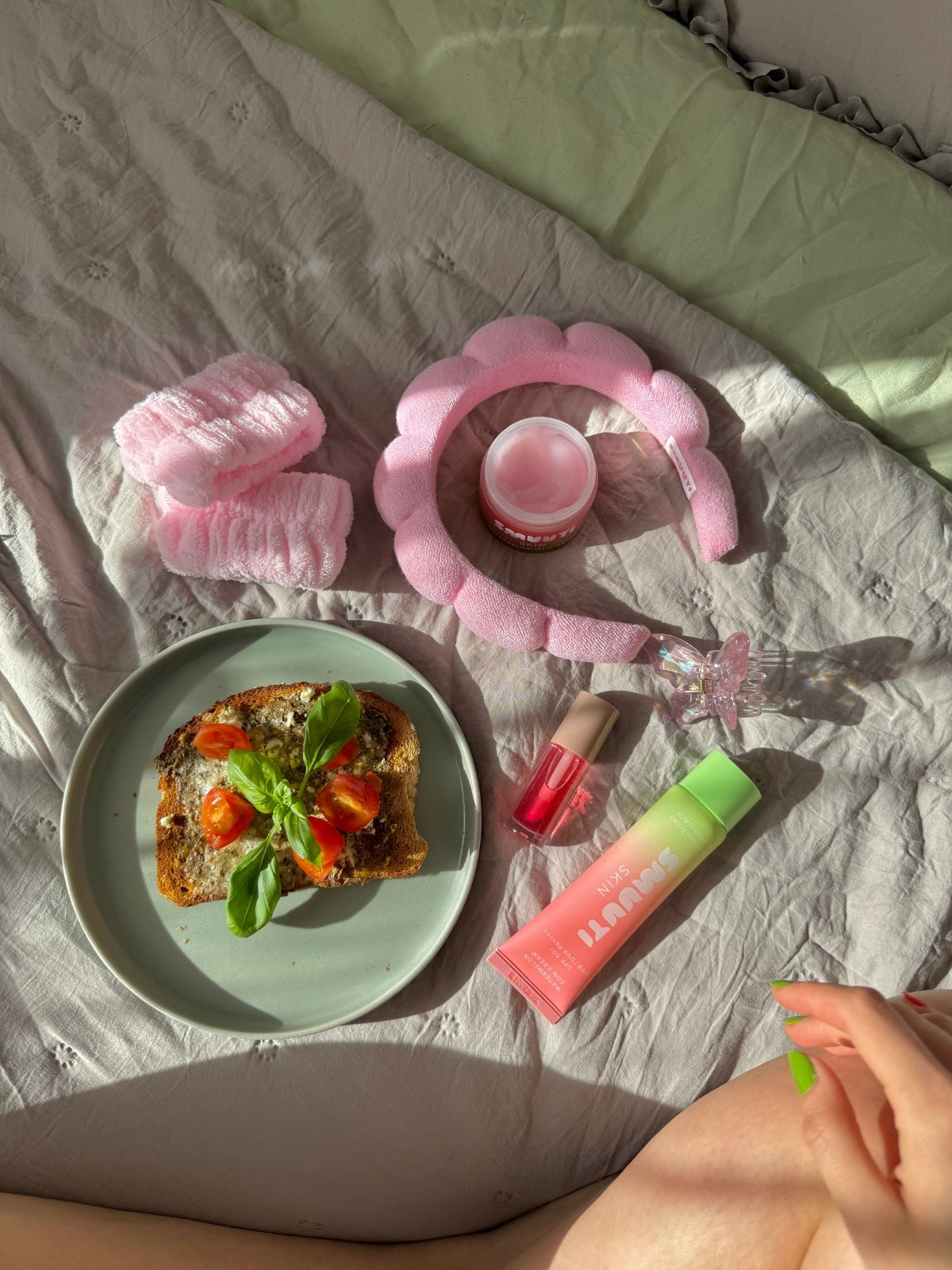 Plate of toast with tomatoes and basil on a bed with Smuuti Skin watermelon sun cream and hair band and wrist cuffs