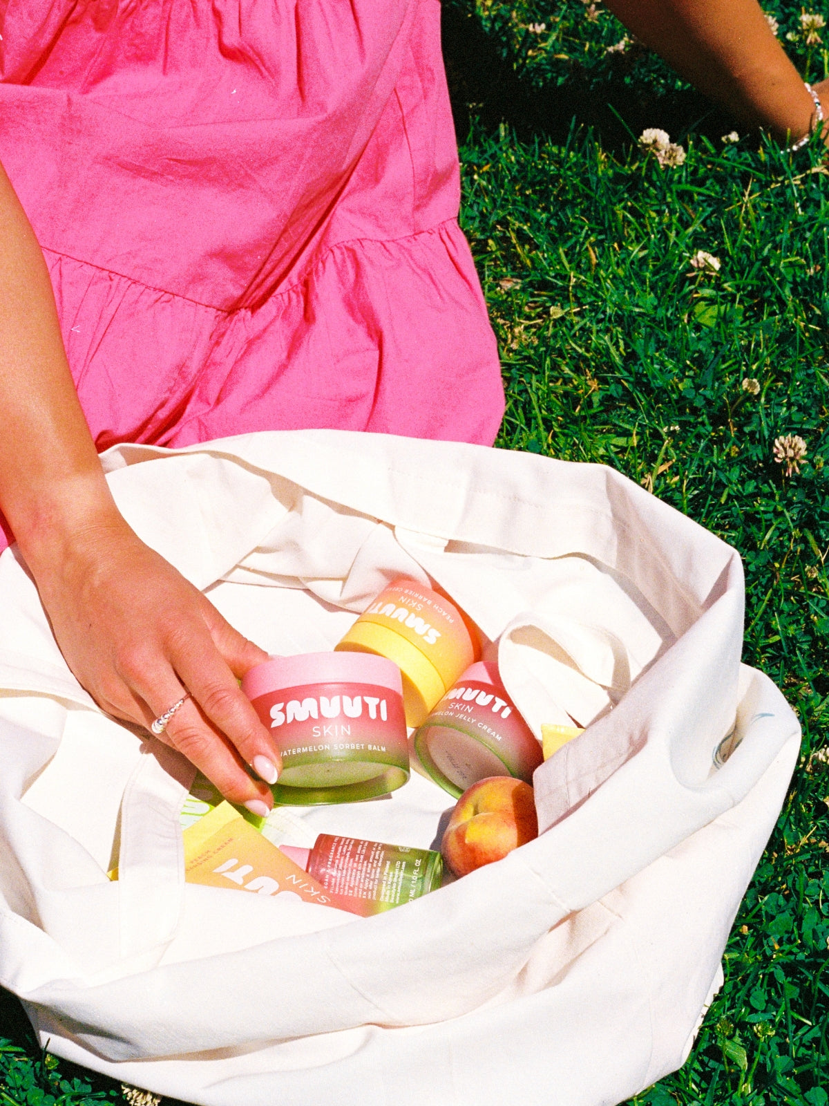 Person holding a white tote bag with Smuuti Skin skincare products on grass