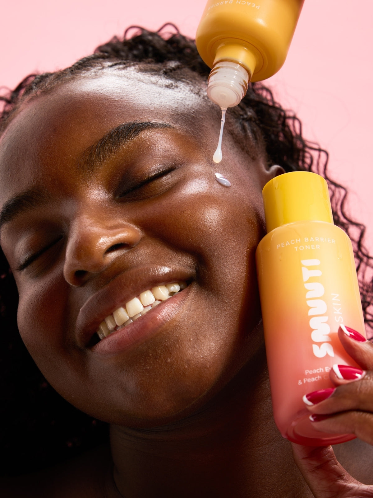 Person applying Smuuti Skin peach barrier toner to their face on a pink background.