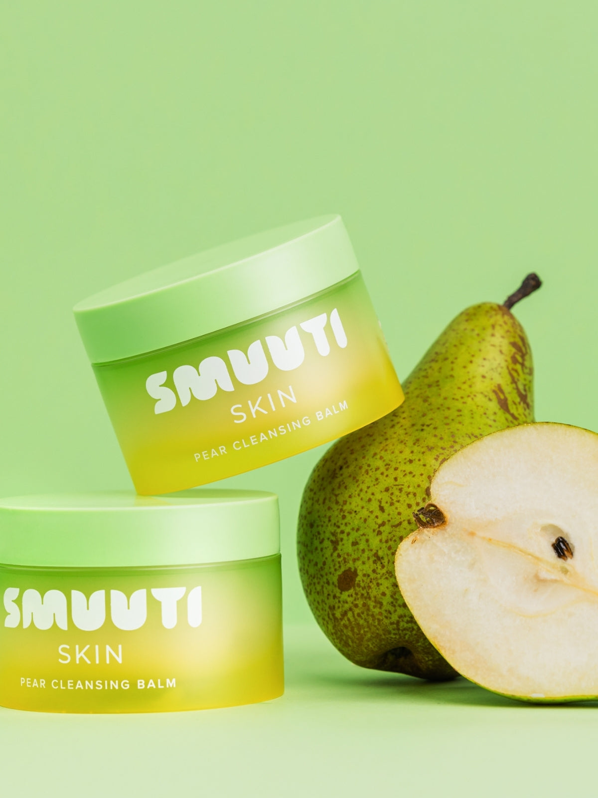 Two jars of SMUUTI Skin Pear Cleansing Balm with a whole and sliced pear on a green background