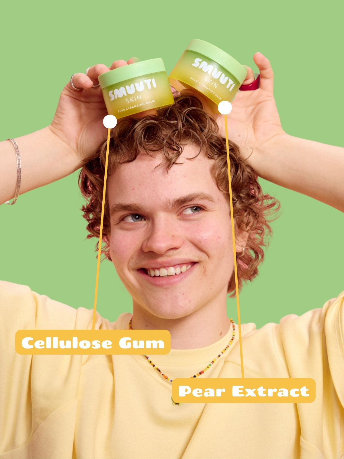 Person holding two jars of Smuuti Skin pear cleansing balm with texts 'Cellulose Gum' and 'Pear Extract' against a green background