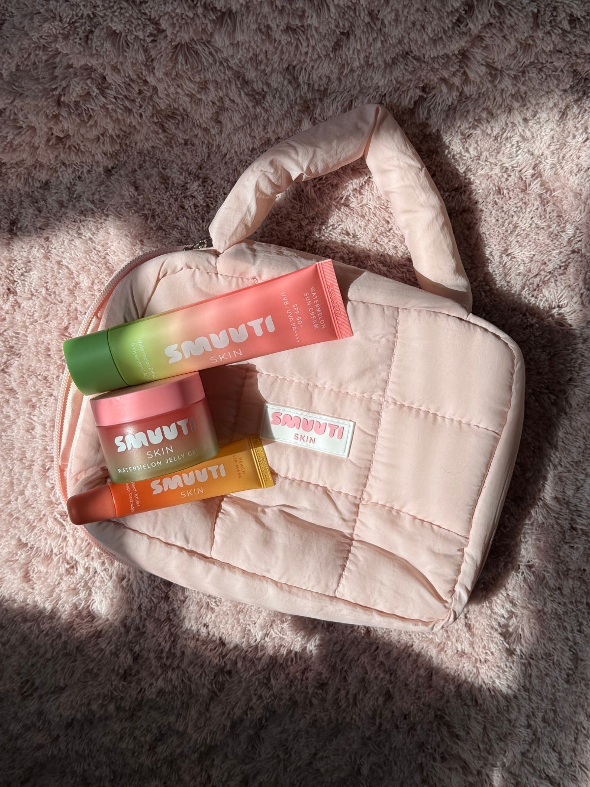 SMUUTI skincare products and puffy cosmetic bag on a gray textured surface