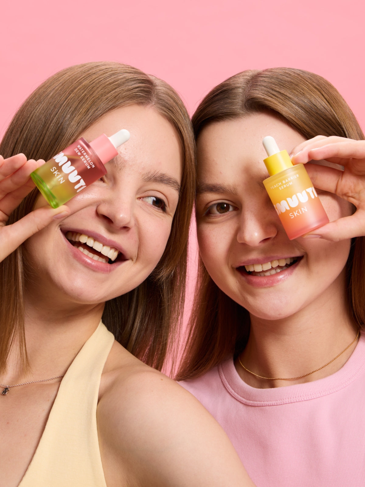 Two models holding Smuuti Skin watermelon dew serum and peach barrier serum against a pink background