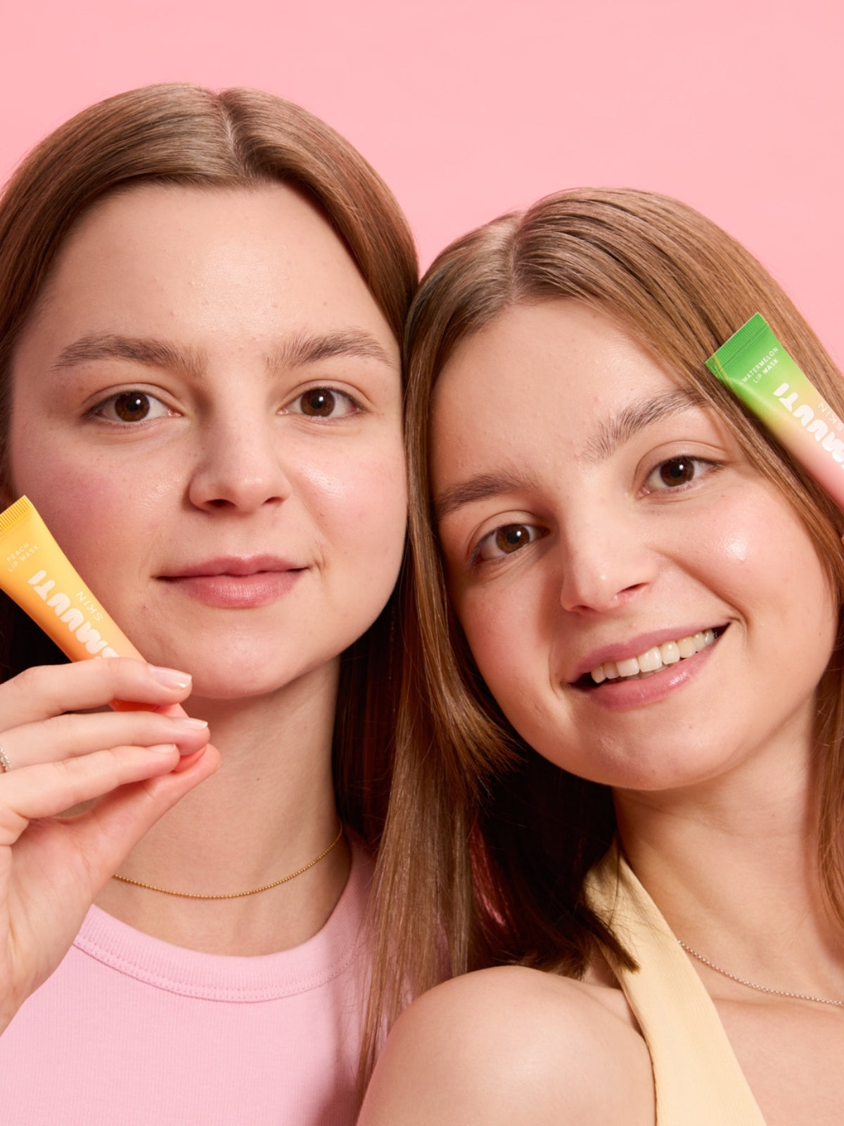 Two women holding colorful lip masks against a pink background