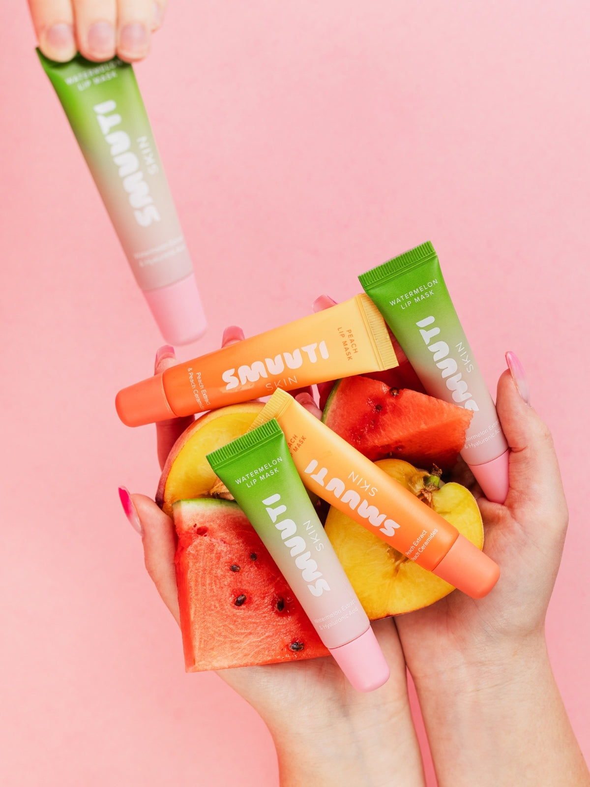 Smuuti Skin lip masks held over fruit slices on a pink background
