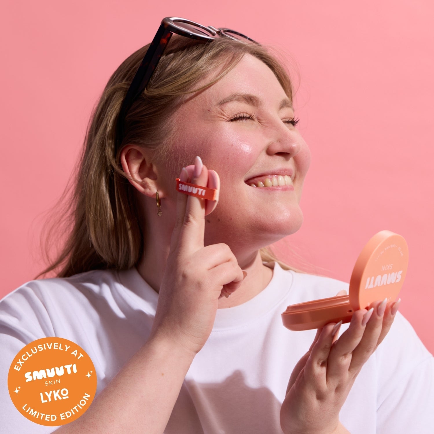 Woman applying sunscreen with peach sun cushion against a pink background