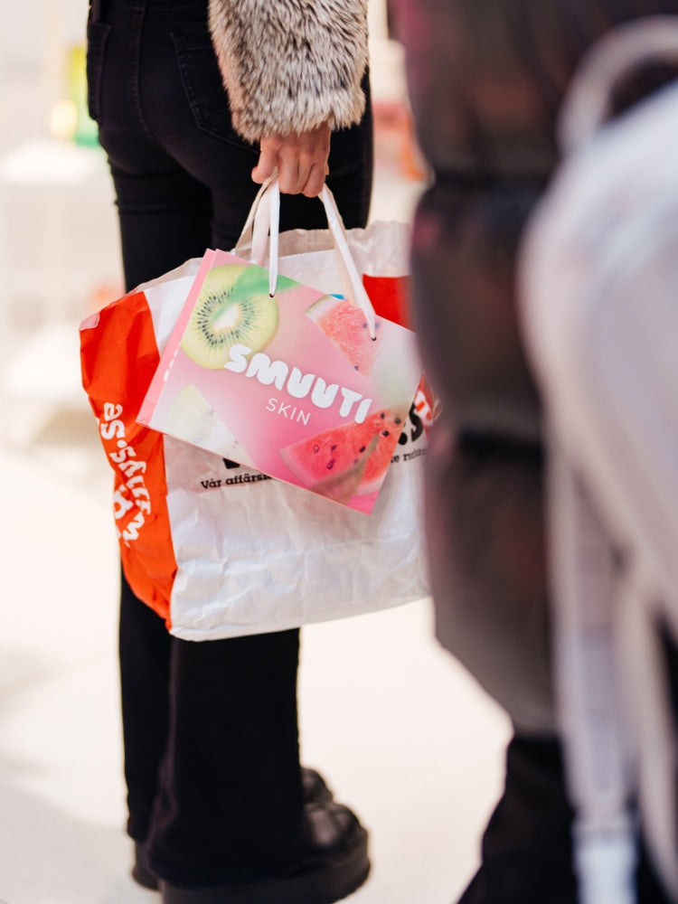 Person holding a shopping bag with colorful graphics and the Smuuti Skin logo.
