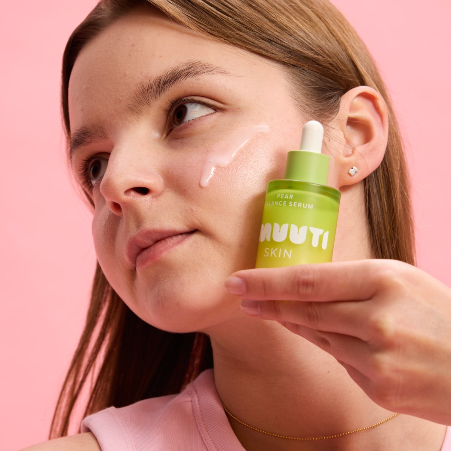 Woman applying smuuti skin pear balance serum to her face with a pink background