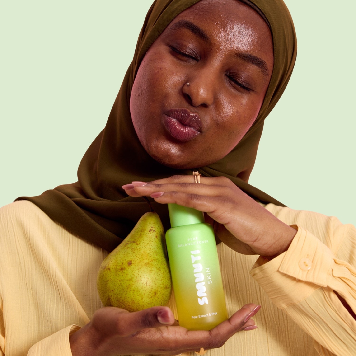 Woman holding a pear and smuuti skin pear balance toner against a light green background
