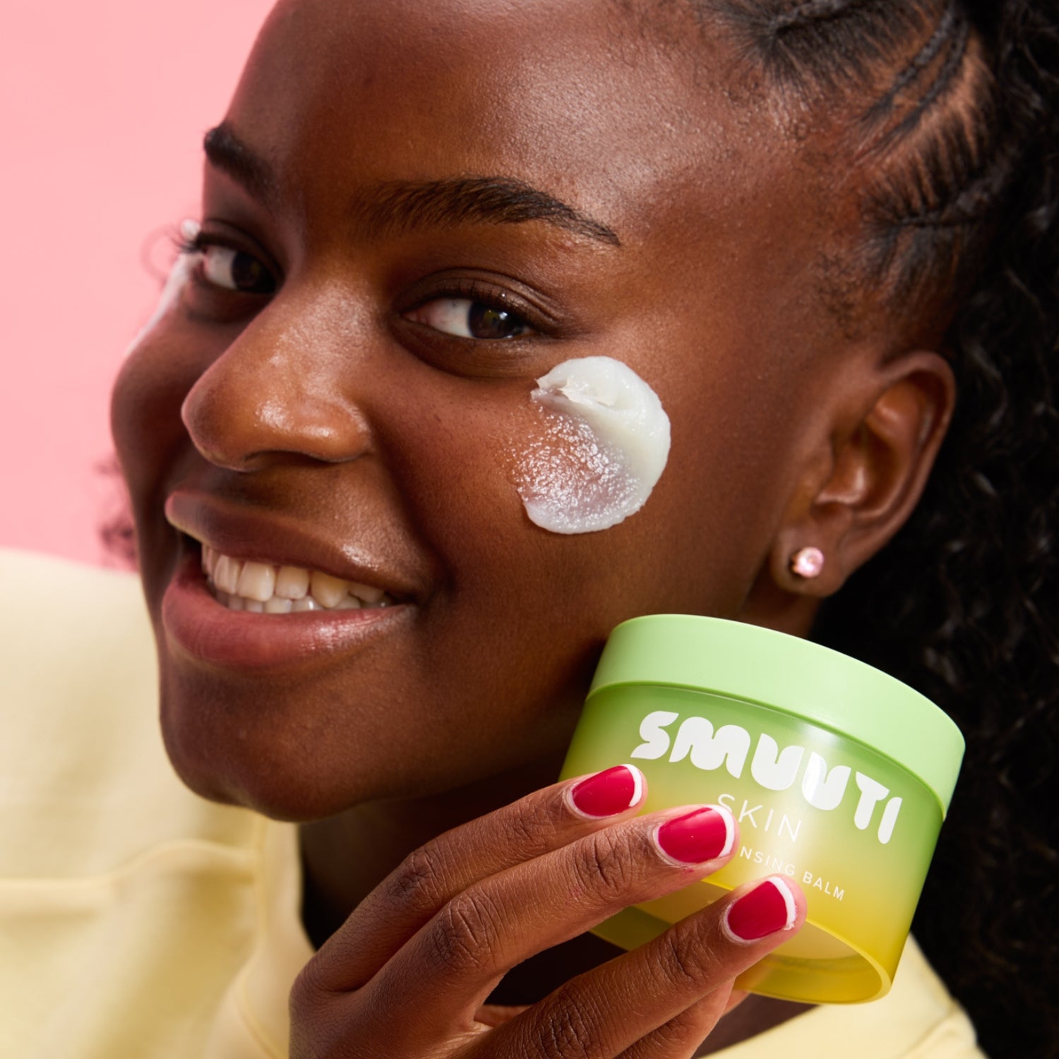 Woman applying smuuti skin pear cleansing balm to her face with a pink background