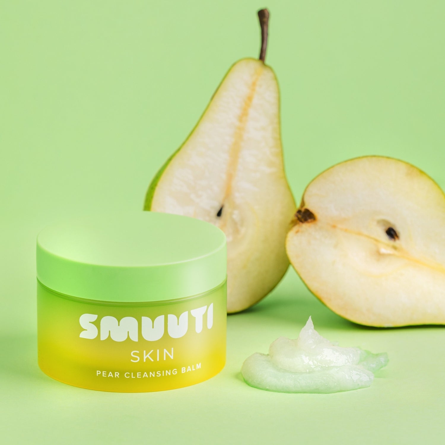 Jar of SMUUTI Skin Pear Cleansing Balm with a pear and its half on a green background