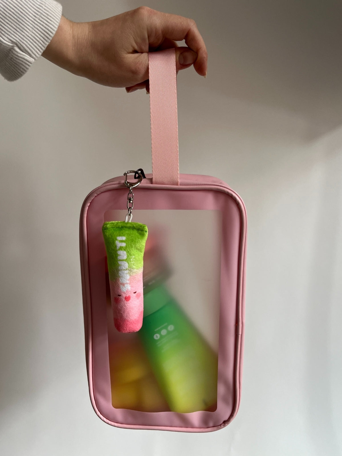 Pink travel pouch with a pink Smuuti Skin plushie keychain, held by a hand against a neutral background.