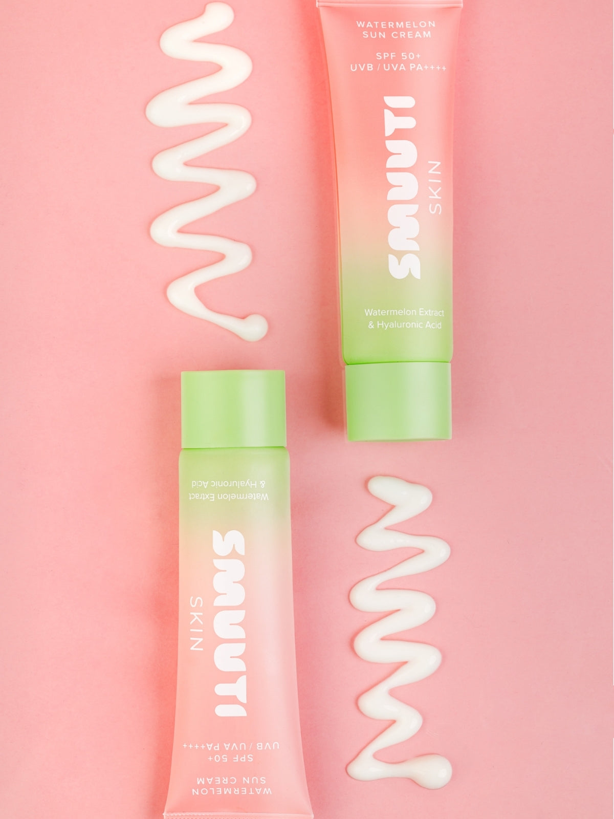 Two tubes of Smuuti Skin watermelon sun cream on a pink background with swirls of sunscreen.