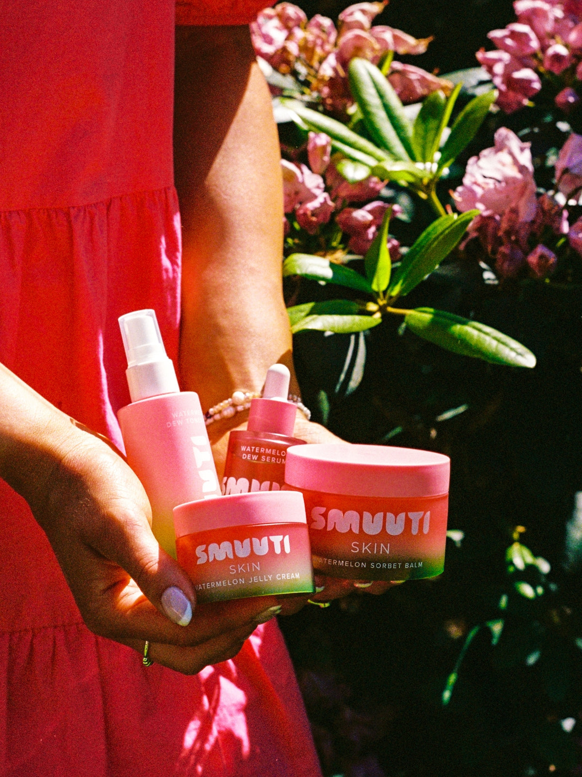 Person holding Smuuti Skin watermelon dew skincare products with pink flowers in the background