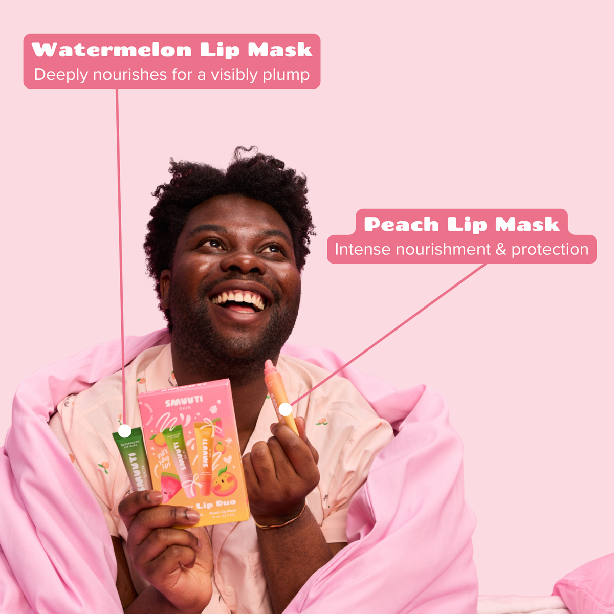 A smiling man wrapped in a pink blanket holds two lip mask