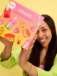 Woman holding a Smuuti Skin Mini Kit with colorful packaging against a yellow background