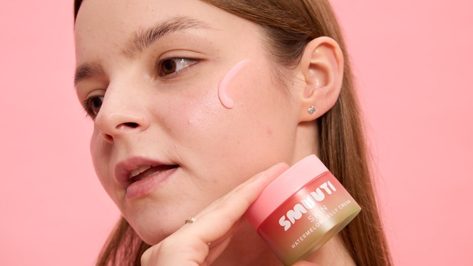 Woman applying a pink cream to her face with a pink background