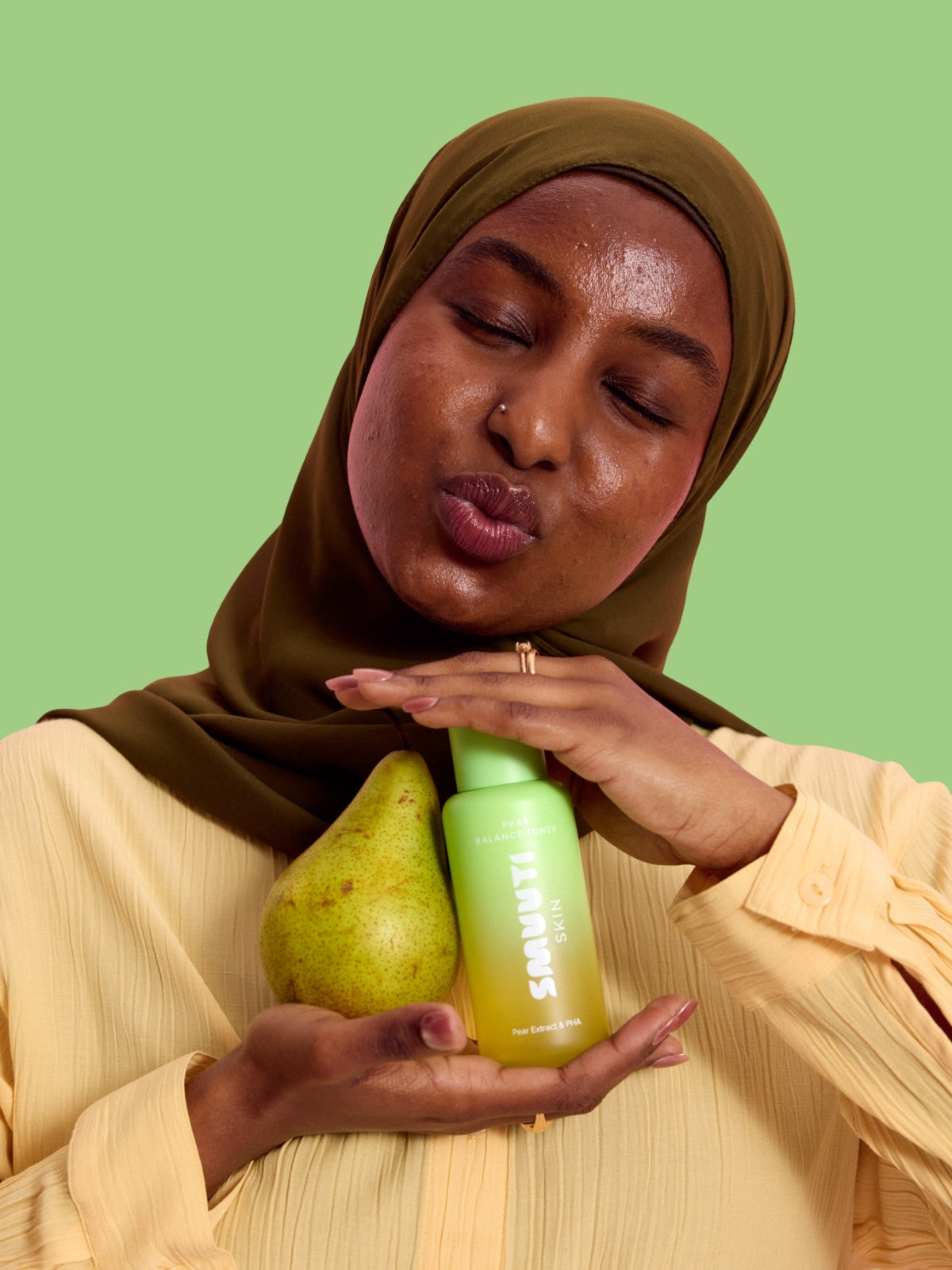 Woman holding a pear and Smuuti Skin pear balance toner against a green background