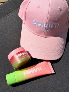 Pink baseball cap and Smuuti Skin skincare products with on a dark surface