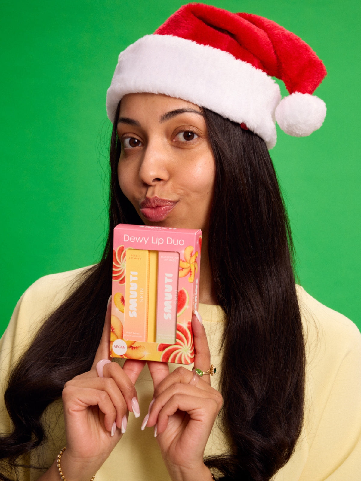 model wearing a Santa hat holding a Smuuti Skin dewy Lip Duo gift set against a green background