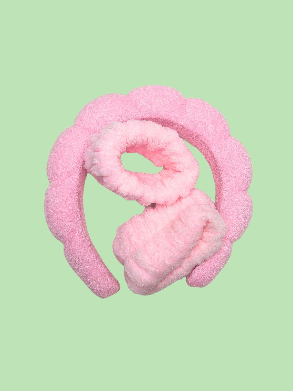 Pink fuzzy headband and wrist cuffs on a light green background