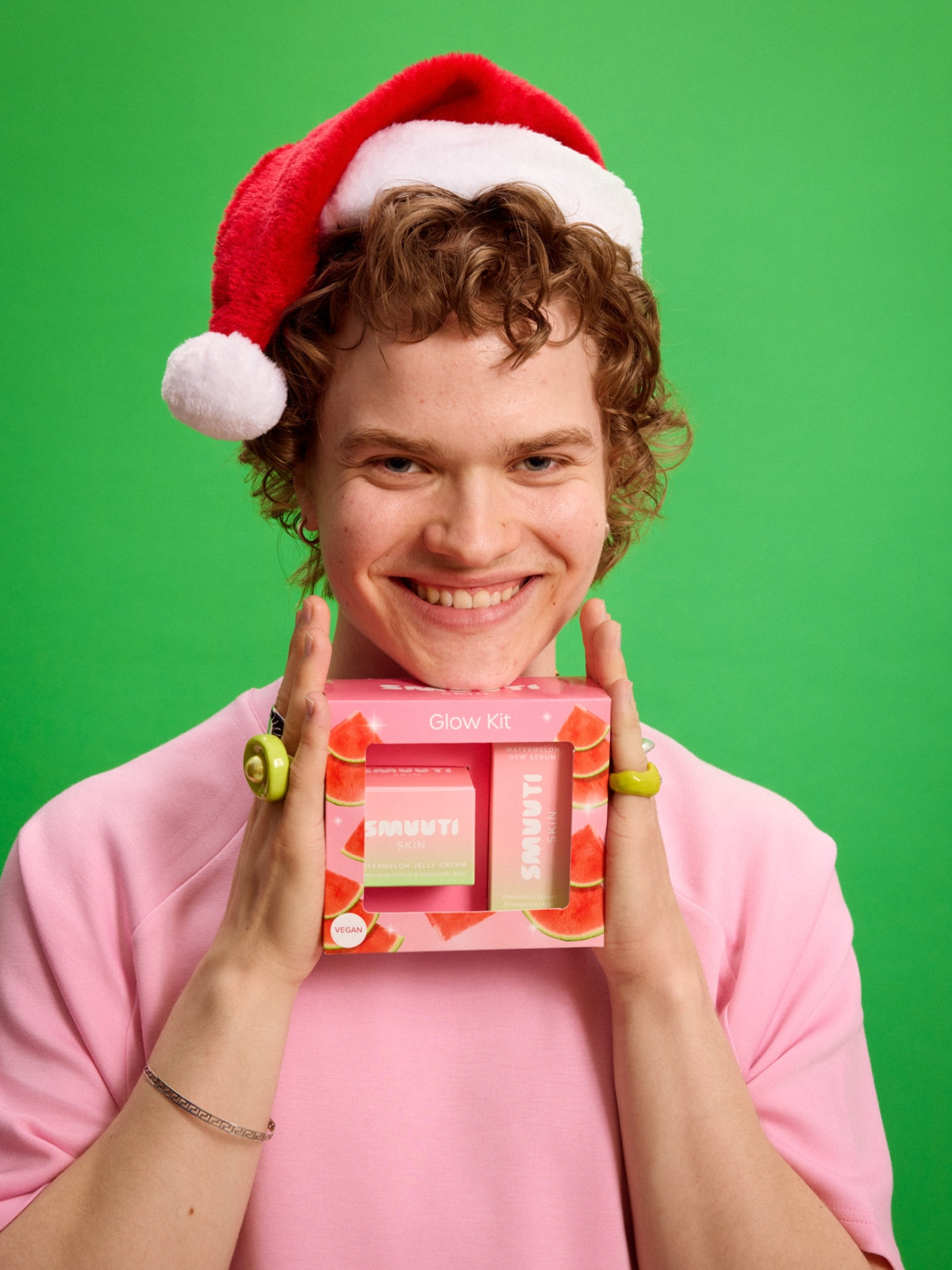 Person wearing a Santa hat holding a Smuuti Skin glow kit against a green background