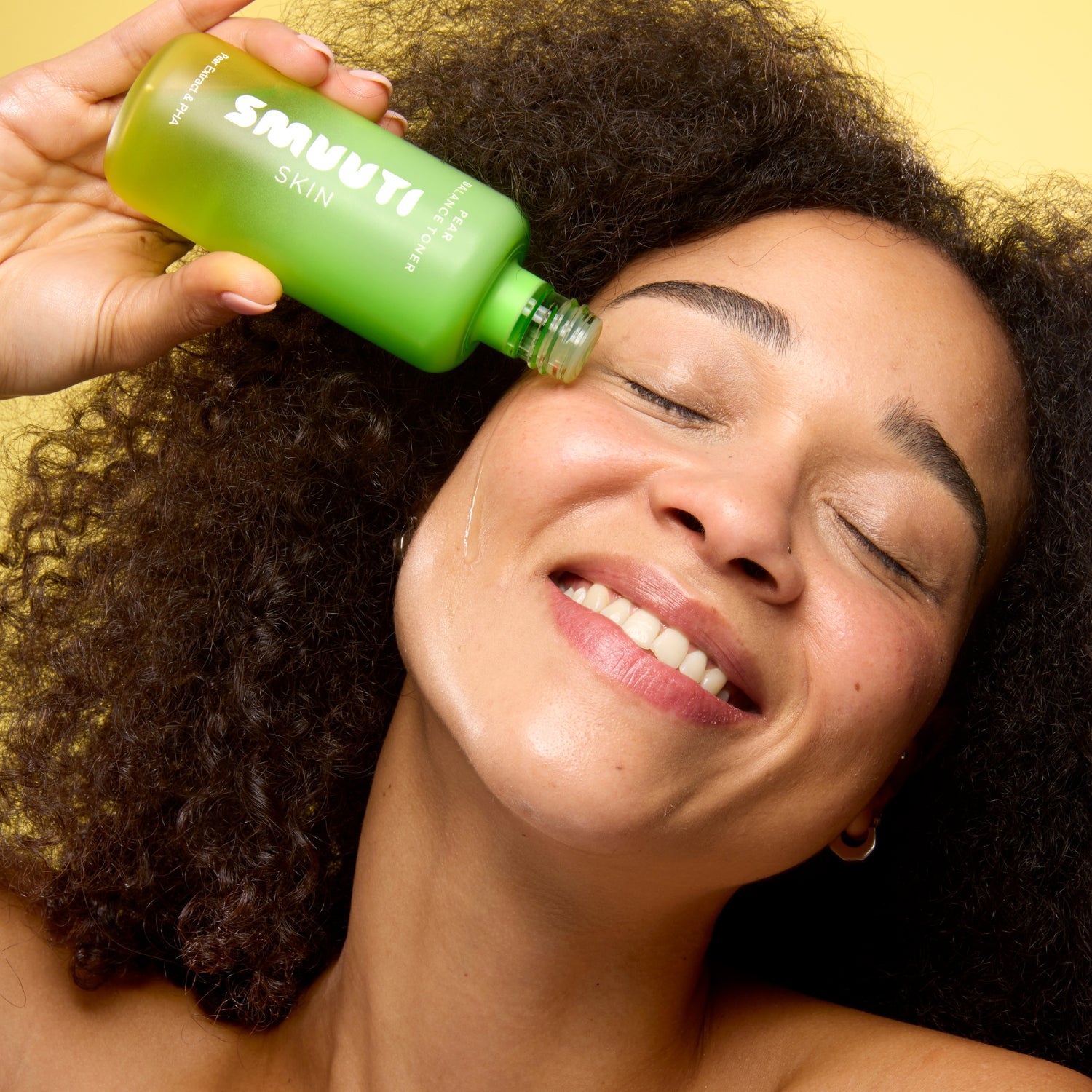 Person applying smuuti skin pear balance toner to their face against a yellow background