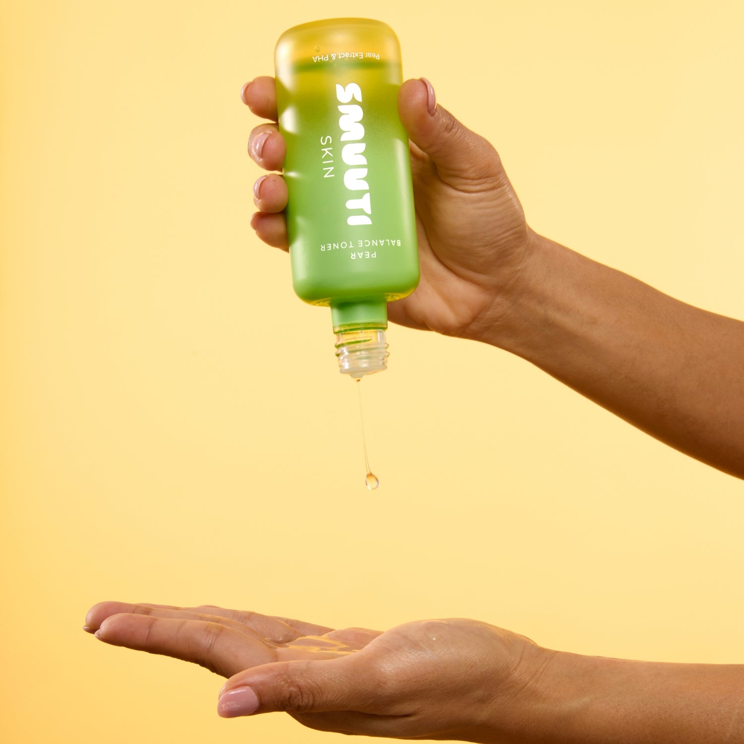 Hand holding smuuti skin pear balance toner dripping onto another hand against a yellow background.