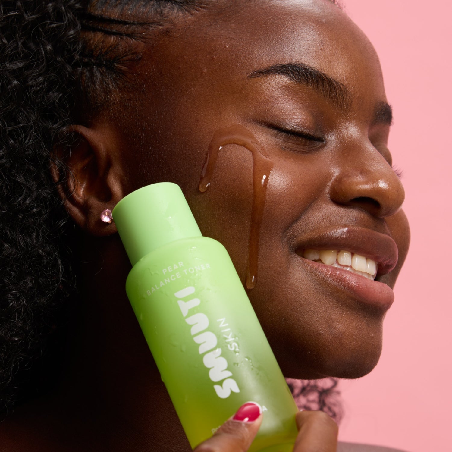 Person applying smuuti skin pear balance toner to their face with a pink background