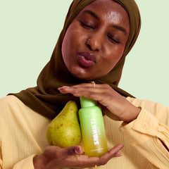 Woman holding a pear and smuuti skin pear balance toner against a light green background