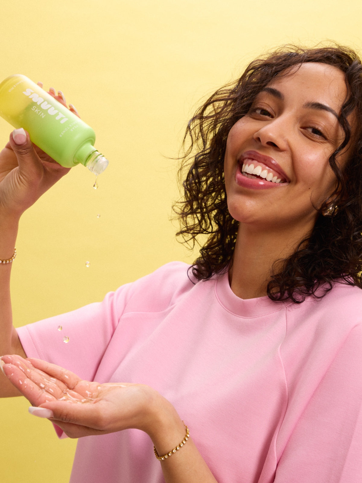 Woman in pink shirt dropping toner onto her hand with a yellow background